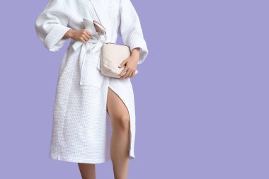 Bornozlu, kozmetik çantalı ve eflatun arka planda modern fotoğraf makinesi olan güzel bir kadın.