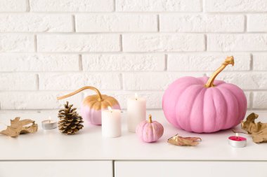 Sonbahar yapraklı pembe balkabakları ve beyaz tuğla duvarın yanındaki çekmecelerde yanan mumlar.