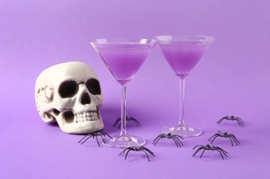 Cadılar Bayramı kutlamaları için kafatası ve örümceklerle mor arka planda lezzetli kokteyller.