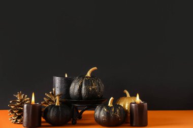 Altın renkli balkabakları ve siyah duvarın yanındaki turuncu masada mumları.