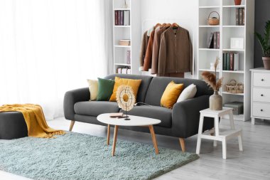 Oturma odasının içinde siyah kanepe ve elbise askısı var.