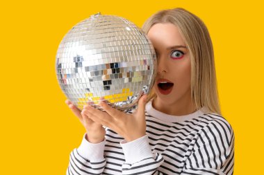 Sarı arka planda disko topu olan güzel, şok olmuş genç bir kadın.