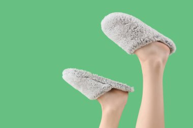 Yeşil arka planda yumuşak terlikler giyen kadın bacakları.