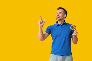 Güzel kurabiyeli yakışıklı adam sarı arka plandaki bir şeyi işaret ediyor.