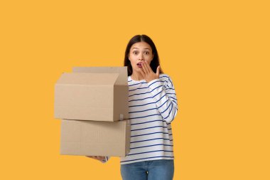 Sarı arka planda açık paket ile şok olmuş genç bir kadın.