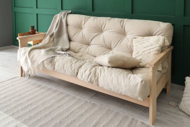 Yeşil duvarın yanında battaniyeli ve yastıklı rahat beyaz kanepe.