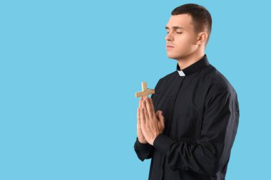 Mavi arka planda dua eden genç bir rahip.