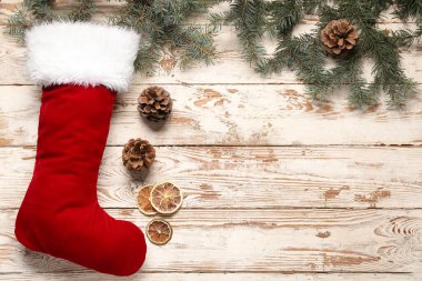 Noel çorabı, köknar dalları, koniler ve beyaz ahşap arka planda kurutulmuş portakal.