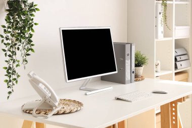 Blank computer monitor with telephone on table in light office