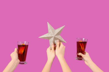 Sıcak şarap kadehleriyle kadın elleri ve pembe arka planda Noel yıldızı.
