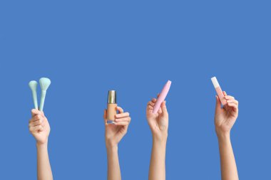 Dekoratif kozmetik ürünleri ve renk arkaplanda makyaj fırçaları olan kadın elleri