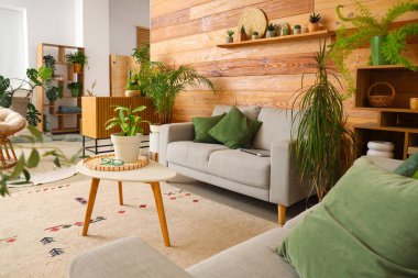 Oturma odasının içinde yeşil bitkiler, kanepeler ve masa var.