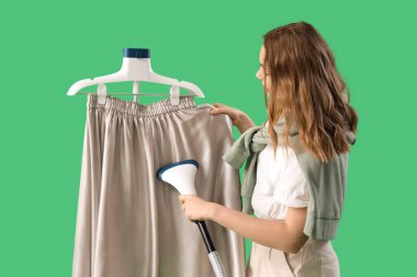 Yeşil arka planda modern giysi buharı olan güzel genç bir kadın.