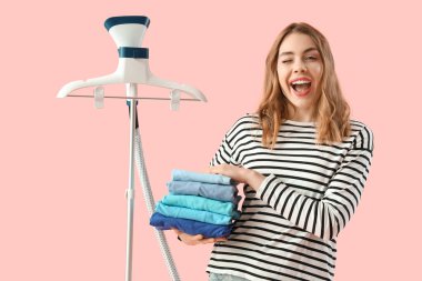 Modern elbise buharlı ve pembe arka planda bir yığın temiz elbisesi olan güzel bir kadın.