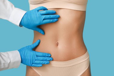 Düz göbekli genç bir kadın ve mavi arka planda plastik cerrah, yakın plan.