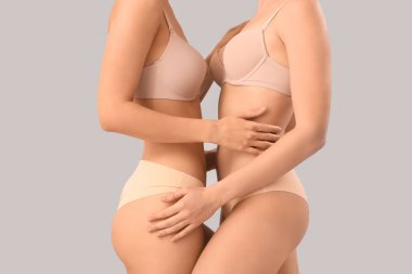 Gri arka planda, şık bej iç çamaşırlı güzel genç kadınlar, yakın plan