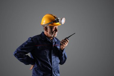 Gri arka planda iki yönlü telsizi olan olgun madenci.