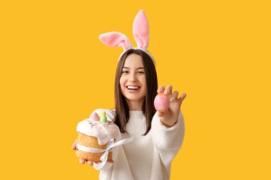 Tavşan kulaklı güzel bir kadın, sarı arka planda Paskalya pastası ve yumurta.