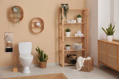 Ev bitkilerinin ve bej duvarın yanında seramik klozetin bulunduğu şık bir banyo.