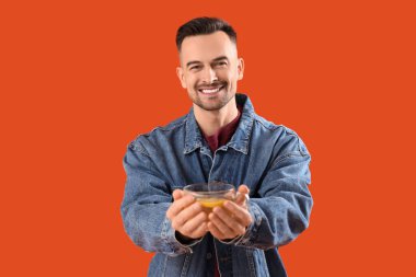 Turuncu arka planda bir fincan limon çayı olan yakışıklı bir adam.