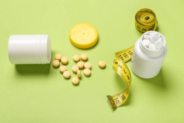 Kilo verme hapları ve yeşil arka planda şerit bulunan şişeler.