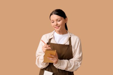 Kahverengi arka planda defter ve kalemle güzel bir garson kız.