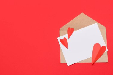 Zarfta boş kart ve kırmızı zemin üzerinde kağıt kalpler var. Sevgililer Günü kutlaması