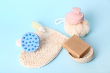 Saç derisi masaj aletleri, şampuan barı, bir şişe kozmetik ürün ve mavi arka planda banyo süngeri.