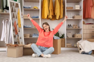 Giysi kutuları ve şık kıyafetleri olan güzel, genç bir kadın soyunma odasında oturuyor.