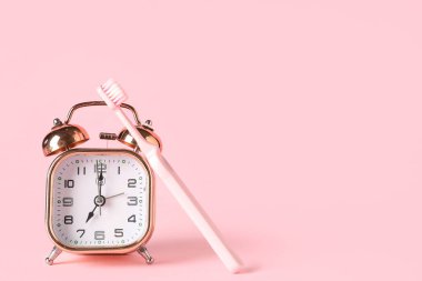 Pembe arka planda çalar saat ve diş fırçası