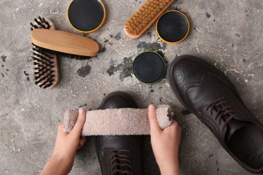 Hands cleaning shoes with cloth on grey grunge background