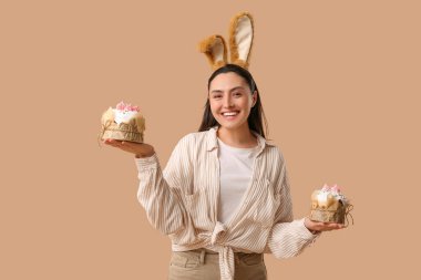 Kahverengi arka planda Paskalya pastaları olan tavşan kulaklı güzel bir genç kadın.