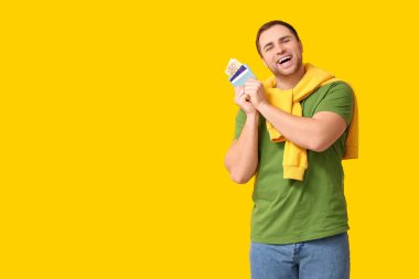 Sarı arka planda kredi kartları olan mutlu genç bir adam cüzdanı tutuyor.
