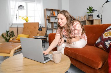 Kırmızı kanepede dizüstü bilgisayar kullanan genç bir kadın.