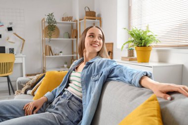 Genç ve güzel bir kadın, oturma odasındaki kanepede dinleniyor.