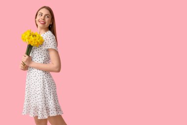 Pembe arka planda bir buket nergis çiçeğiyle mutlu genç bir kadın.