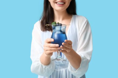 Elinde bir bardak lezzetli kokteyl ve mavi arka planda yabanmersini tutan genç bir kadın.