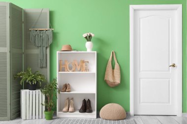 Salonun içinde raf ünitesi, bir buket çiçek ve yeşil duvarda çanta.