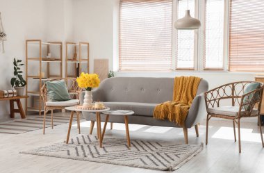 Gri kanepe, halı, sehpa ve narsisli vazo ile oturma odasının içinde.