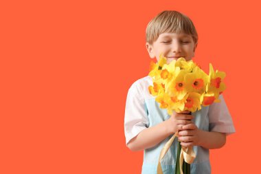 Cute little happy boy with bouquet of beautiful narcissus on orange background