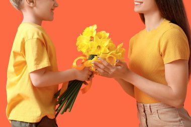 Oğlum mutlu annesine turuncu arka planda bir buket narsisle selam veriyor.