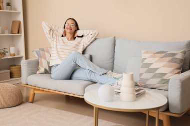 Happy young woman sitting on grey sofa in light living room