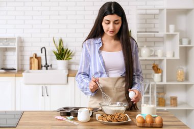 Güzel, genç bir kadın mutfakta çikolatalı kurabiyeler için hamur hazırlıyor.
