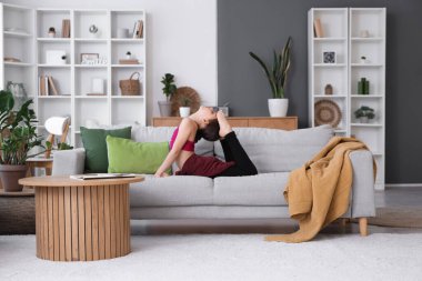 Evdeki kanepede jimnastik yapan küçük kız.