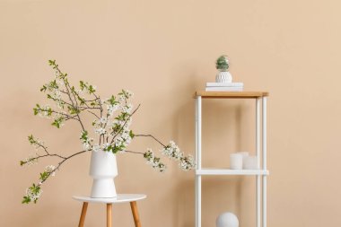 Sehpanın üzerinde, bej odadaki raf ünitesinin yanında çiçek açan bir vazo.
