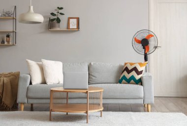 Interior of stylish living room with floor electric fan and laptop