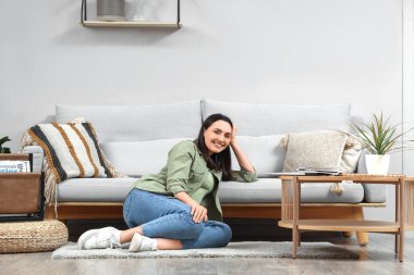 Evdeki gri kanepenin yanında oturan genç kadın.