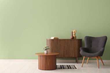 Siyah koltuk, sehpa ve yeşil duvarın yanındaki çekmeceler.