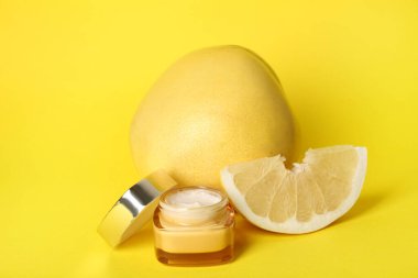 Sarı arka planda bir kavanoz kozmetik ürünü ve taze pomelo, yakın plan.