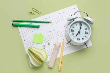 Yeşil arkaplanda alarm saati ve ofis kırtasiyesine sahip takvim
